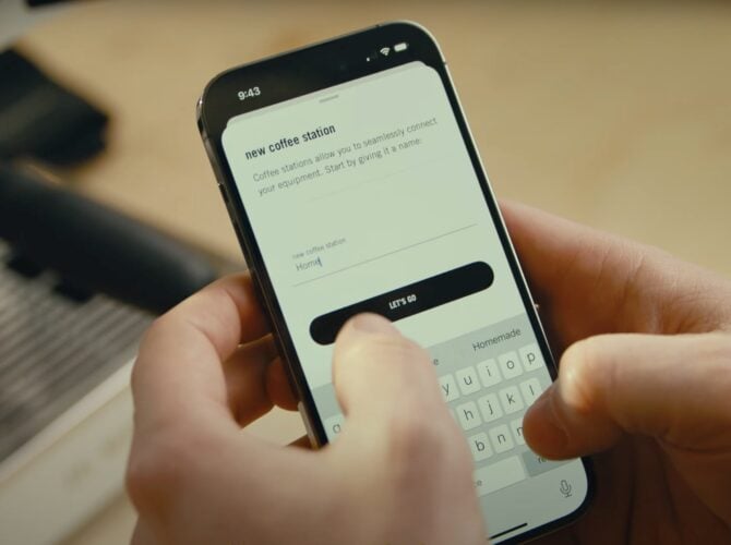 Person using smartphone to enter name for new coffee station setup, with on-screen prompt and keyboard visible